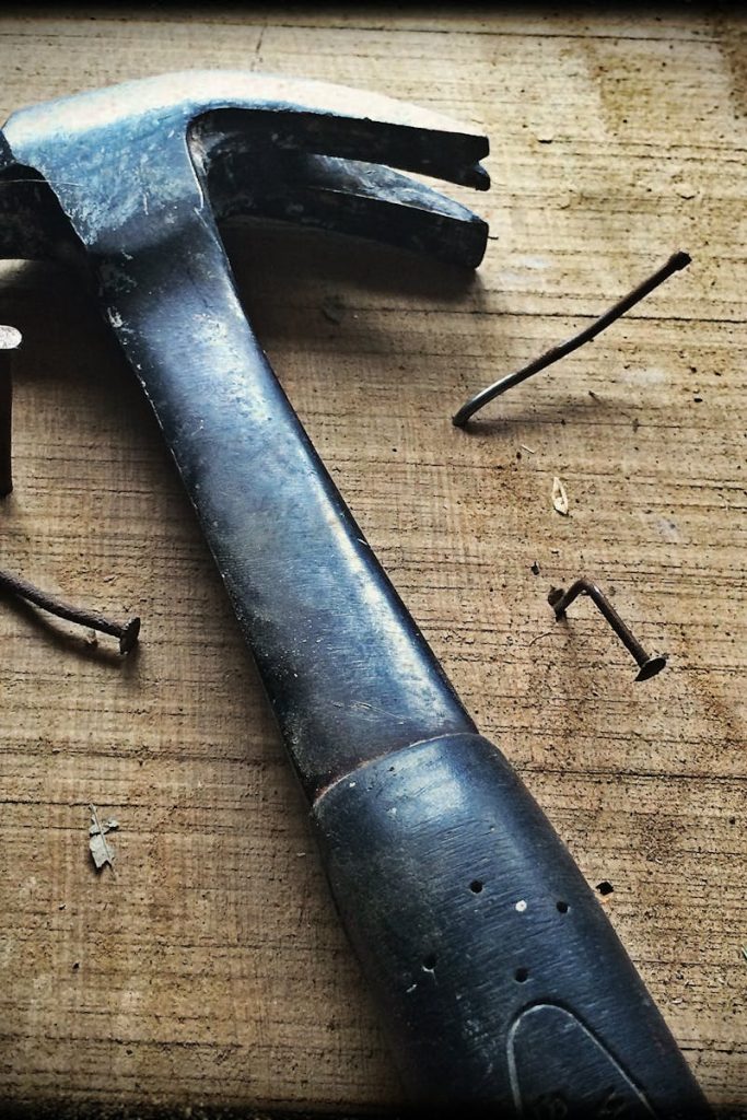 A weathered hammer surrounded by bent nails on a wooden plank, capturing the essence of carpentry work.