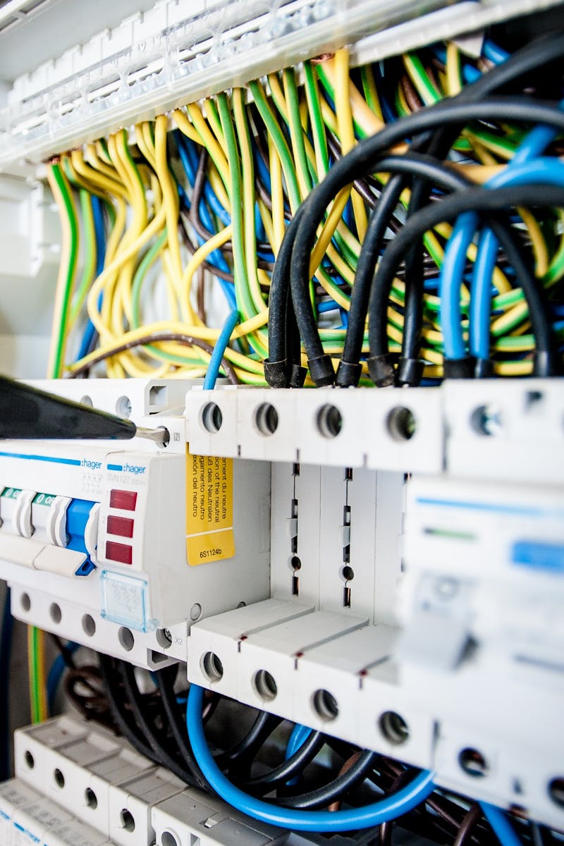 Hand of electrician working on a circuit breaker panel with colorful wires, ensuring safe electrical connections.