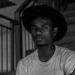 Black and white portrait of a young man in a hat sitting on stairs.
