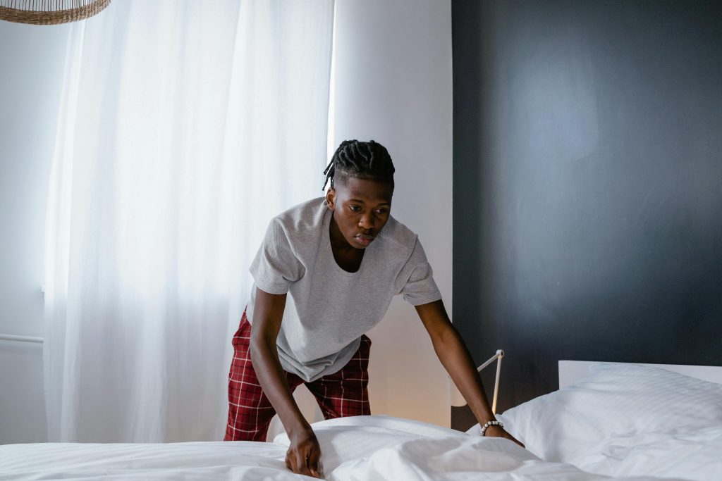 A young man organizing a bed in a modern room, focusing on tidiness and housekeeping.