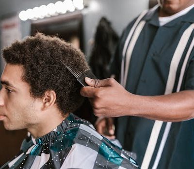 A barber uses an afro pick to style a client's hair in a modern barbershop setting.