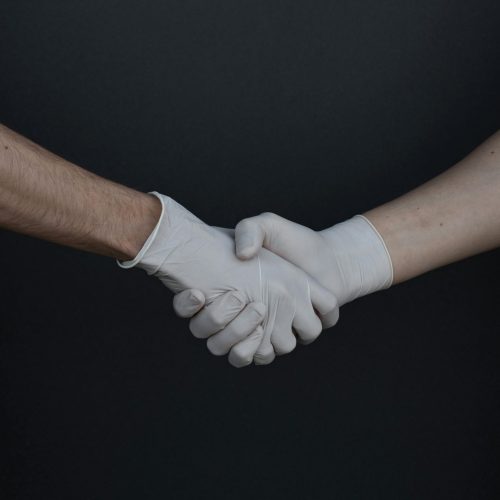 Two people shaking hands while wearing latex gloves, illustrating safety and protection.